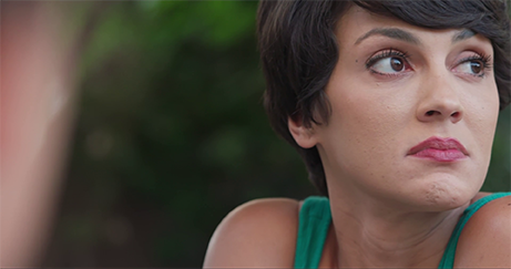 Close-up shot from the movie “An Unquiet Mind” of a woman with short dark hair and a green top, looking pensively to her right.