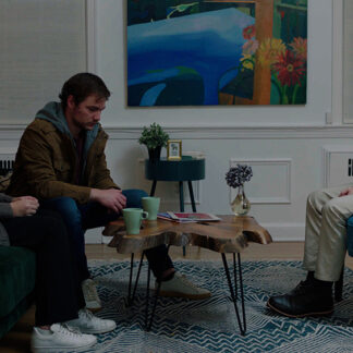 In a stylishly designed room, a distressed couple sits across from a man perched on the edge of his seat, his expression intense and contemplative, as if carefully weighing his next words.