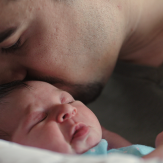 a father gently kissing his newborn baby on the head.