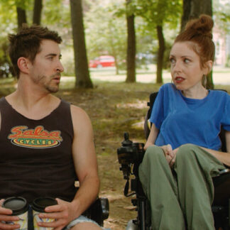 A woman in a wheelchair looking astonishingly at a man sitting on a bench in a wooded park.